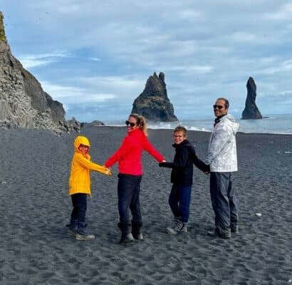 Family smiling and holding hands on black sand beach in Iceland