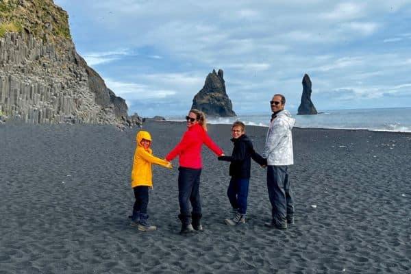 Family smiling and holding hands on black sand beach in Iceland