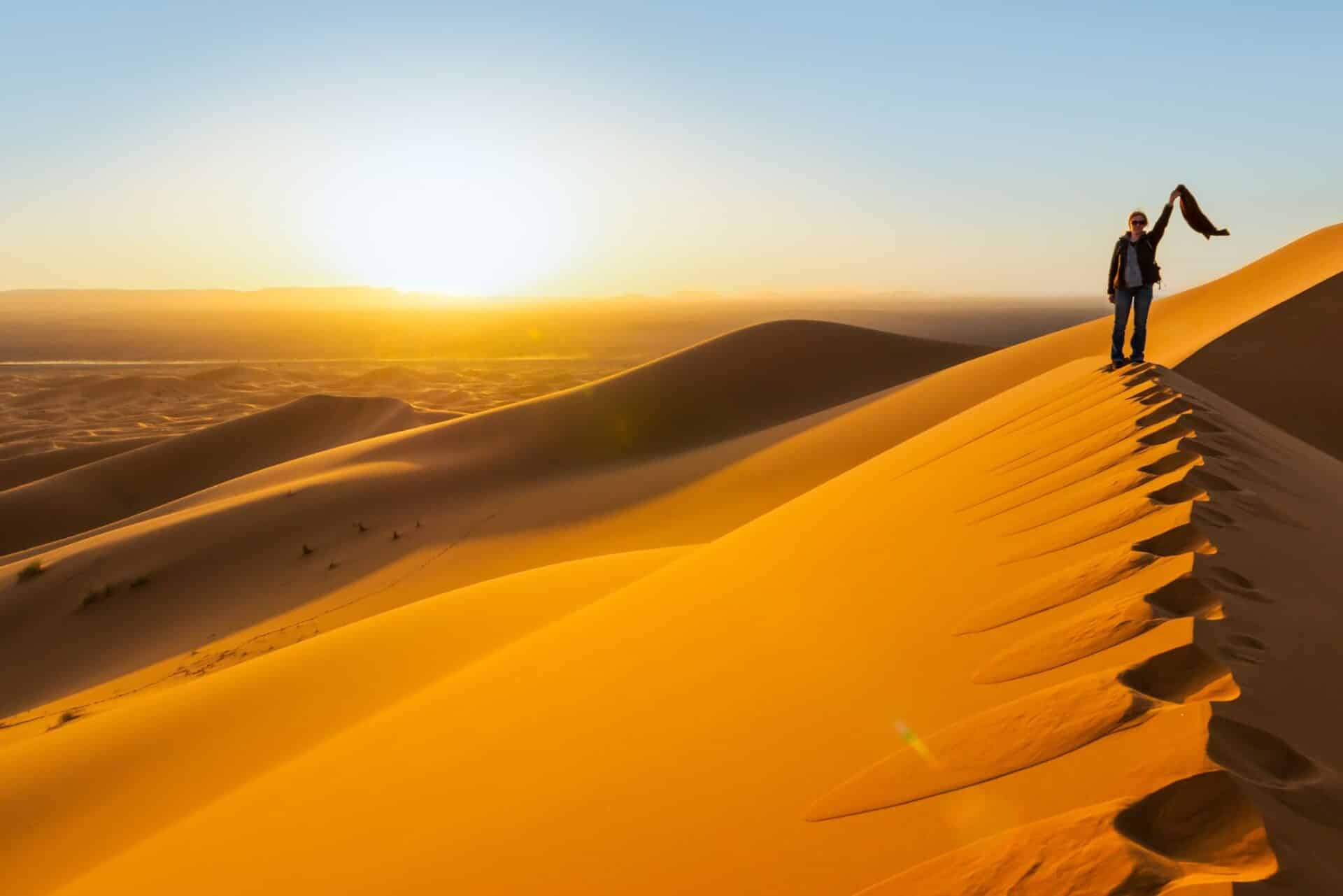 Woman on sand dune waiving a scarf in Sahara Desert, Morocco