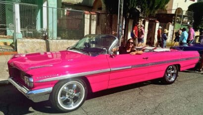 Traveler enjoying a ride in a pink classic car in Havana, Cuba. She's enjoying a Walking tour of Cuba.