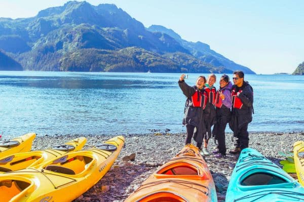 Family near kayaks and water taking a selfie with mountains in the background